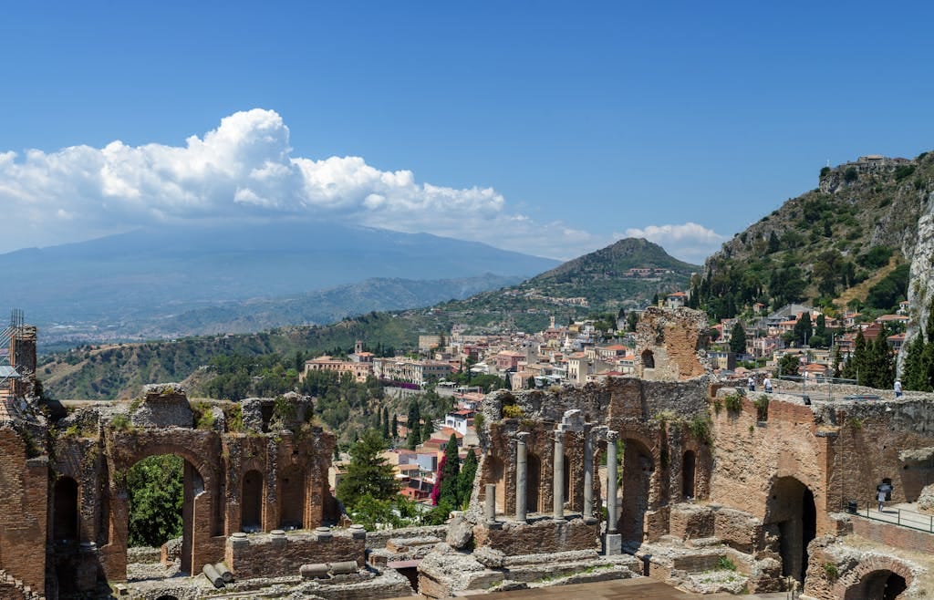 Explore the awe-inspiring ruins of the Ancient Theatre of Taormina, Sicily with Mount Etna in the background.
