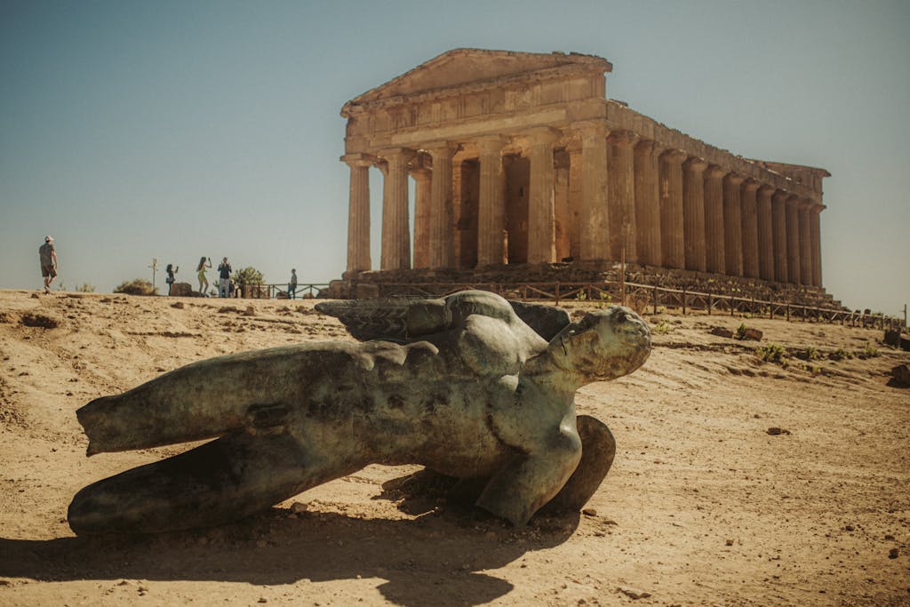 Photo of the Valley of the Temples in Agrigento, Italy featuring a fallen statue against a historical temple.