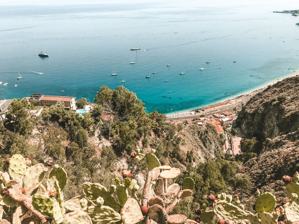 A breathtaking view of the Mediterranean coast with cacti in the foreground and boats dotting the azure sea.