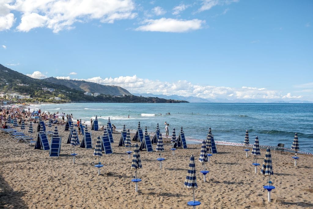 A scenic beach in Sicily, Italy, with rows of umbrellas and people enjoying the sun and sea.