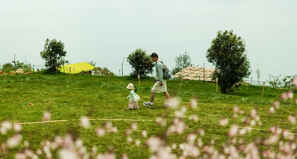 A father and child walking in a lush, green field beside Erhai Lake in Dali, China.